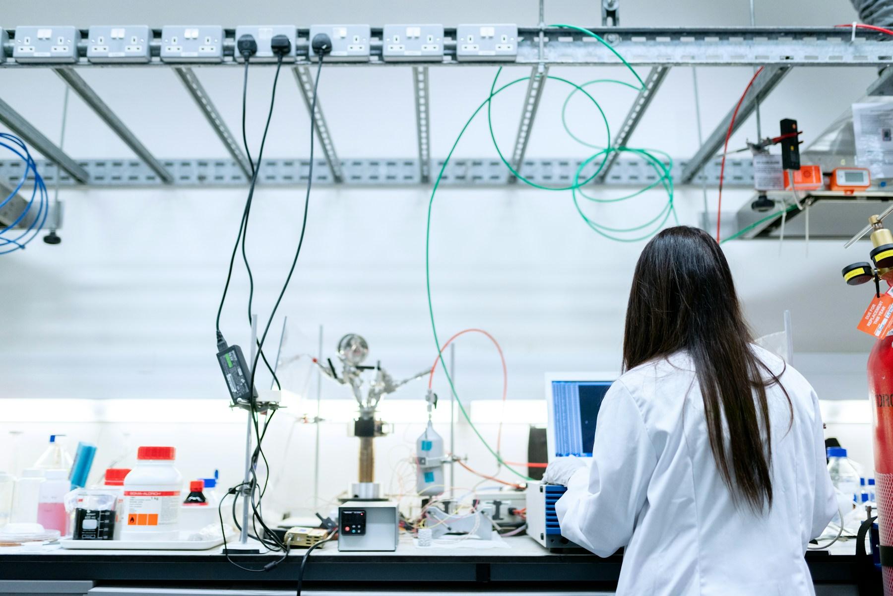 An engineer in a lab coat working at a laptop beside an experimental rig