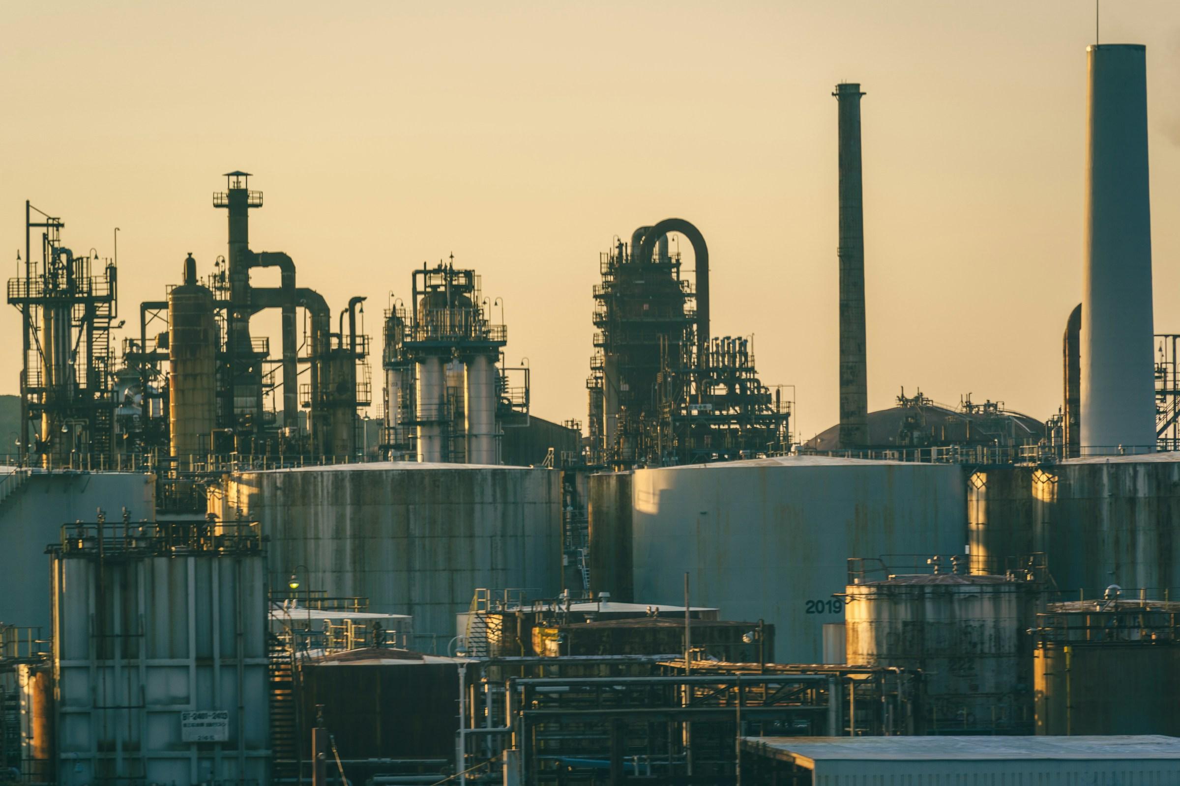 Refinery towers and storage tanks under a soft golden evening sky